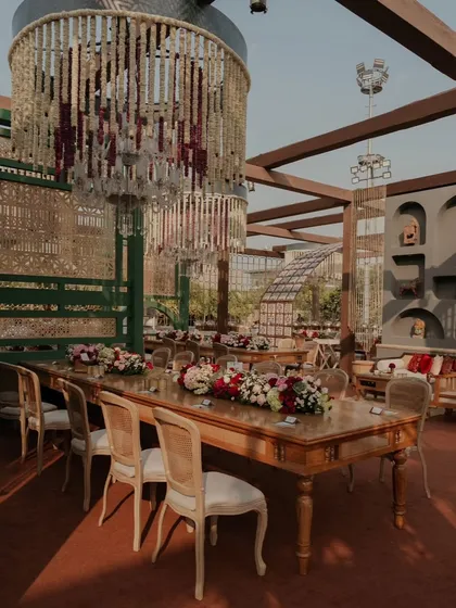 A long table setup for a grand feast. The combination of floral runners, elegant chairs, and overhead chandeliers creates a sophisticated and inviting dining experience.