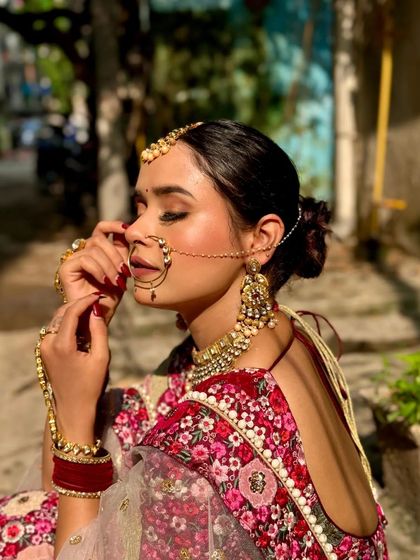 A bride looking serene and beautiful in a floral print sabyasachi-style lehenga. The traditional jewellery, including the nath and maang tikka, completes the look.