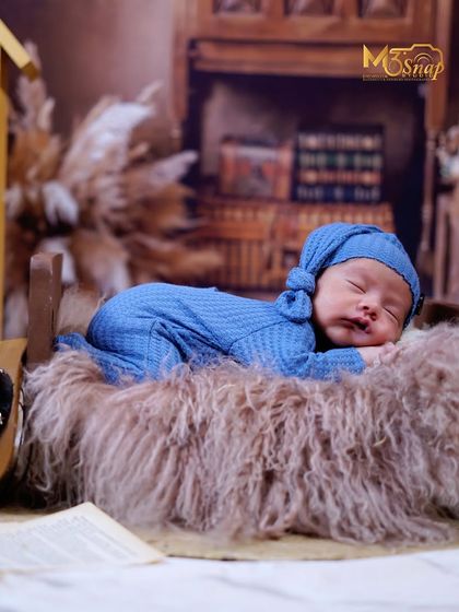 A full-body shot of a newborn sleeping peacefully on a soft fur blanket. The rustic, library-themed backdrop adds a warm and timeless feel to the portrait.