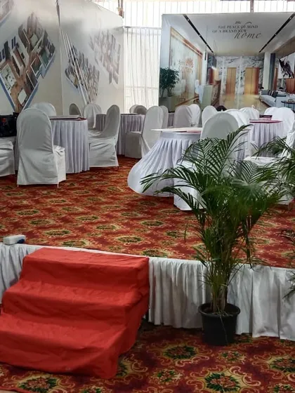 For this corporate setup, I created a raised platform area with a printed backdrop showing the client's project. The space includes carpeted flooring, skirted round tables, and potted plants to complete the look.