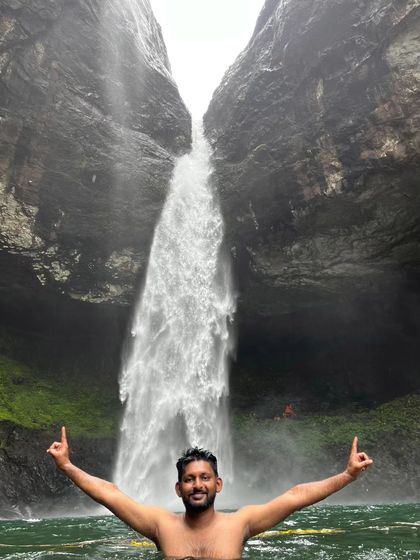A triumphant moment for a trekker enjoying the cool, clear waters of Devkund waterfall.