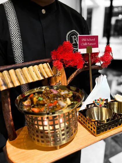 A server presents our Old School Chilli Paneer on a decorative tray. This personalized service adds a touch of sophistication to the dining experience, making guests feel truly special.