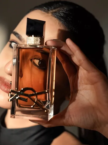 A product-focused shot for a YSL fragrance campaign. The makeup is sharp and elegant, with a defined eye that draws attention, mirroring the luxury and desire of the brand.