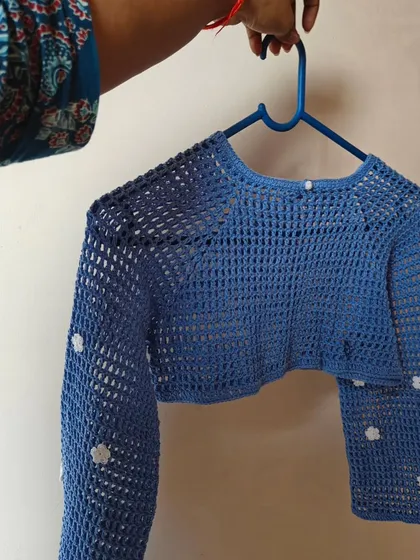 A full view of the blue mesh crop top with long sleeves and delicate daisy accents. The open stitch makes it incredibly light and breathable for warmer weather.
