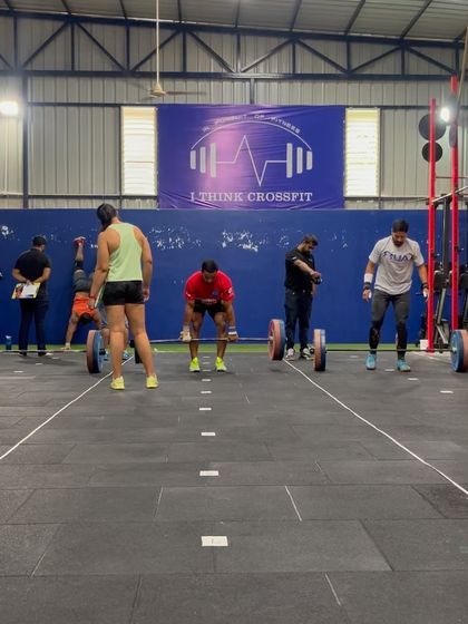 A wide view of the competition floor, with athletes engaged in different parts of a workout, including wall walks and deadlifts.