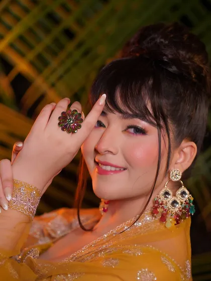 A close-up of the Haldi look, focusing on the colorful eye makeup and flawless skin. The high bun with bangs adds a modern touch.