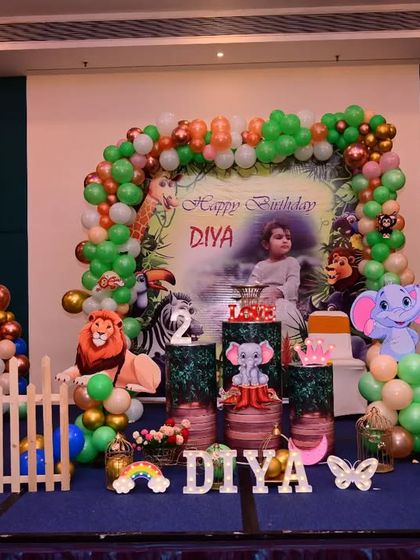 A wide shot of the jungle safari birthday stage decoration. This view shows all the elements together, including the backdrop, balloon arch, animal cutouts, and picket fence.