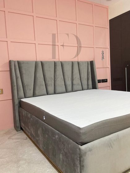A full view of the grey velvet bed against the geometric pink wall. The design is a perfect example of how we balance masculine and feminine design elements to create a harmonious space.