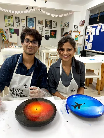A couple proudly displays their resin art, one a galaxy clock and the other a beach scene. It's a great way to explore different themes in one session.
