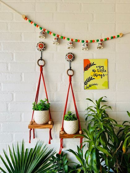 Another beautiful wall arrangement featuring two red macrame wall shelves, a bell bunting, and a wooden frame. This set is perfect for adding a touch of rustic charm and color to your living room or balcony.