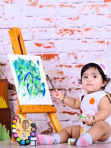 A baby artist painting on a canvas, set against a brick wall for a studio feel.