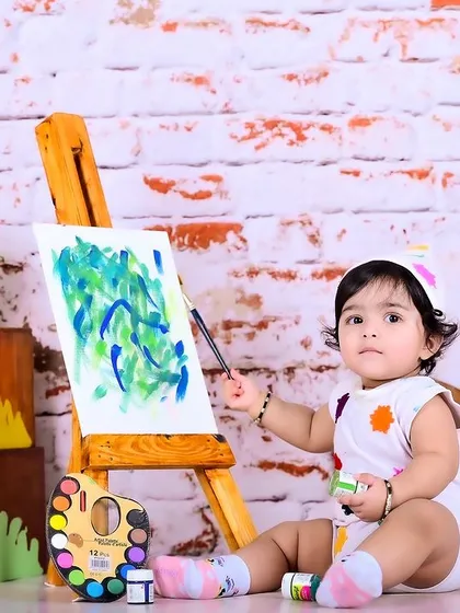 A baby artist painting on a canvas, set against a brick wall for a studio feel.