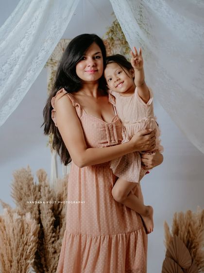 A happy portrait of a mother holding her daughter, who is playfully making a peace sign. This image captures their fun-loving personalities in a beautiful studio setting.