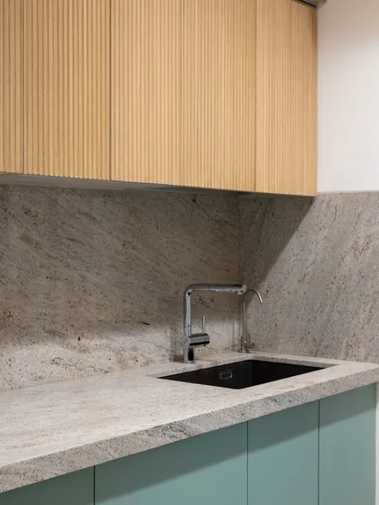 The combination of fluted wood upper cabinets and a speckled quartz countertop creates a kitchen that is rich in texture and visual interest. The undermount sink maintains the clean, modern lines of the space.