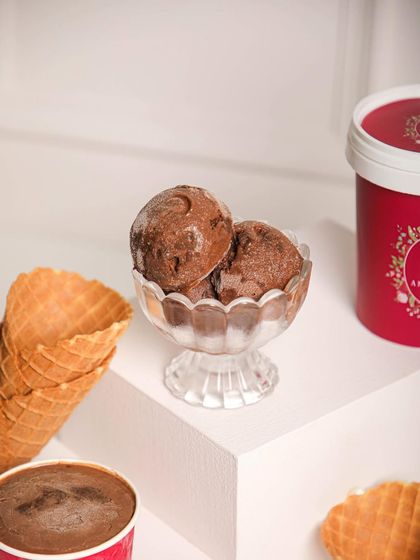 Scoops of rich chocolate ice cream in a glass bowl, with our signature tubs in the background. A classic way to beat the heat.