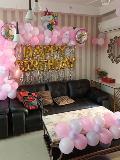 A pink unicorn-themed birthday decoration for a living room. This setup includes a balloon arch over the sofa and a unicorn foil balloon.