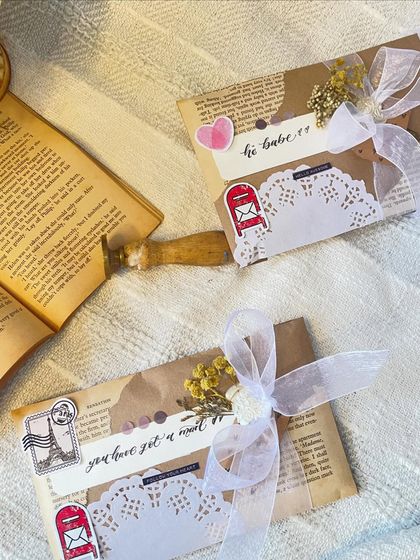 A pair of custom letters ready to be sent out. Each one is decorated differently to match the vibe of the message inside. One has a sweet heart sticker, while the other has a travel theme.