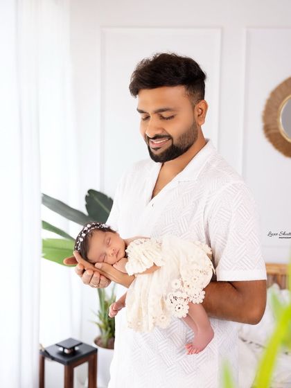 A proud father holding his sleeping newborn daughter in the bright, airy studio. A perfect portrait of a doting dad.