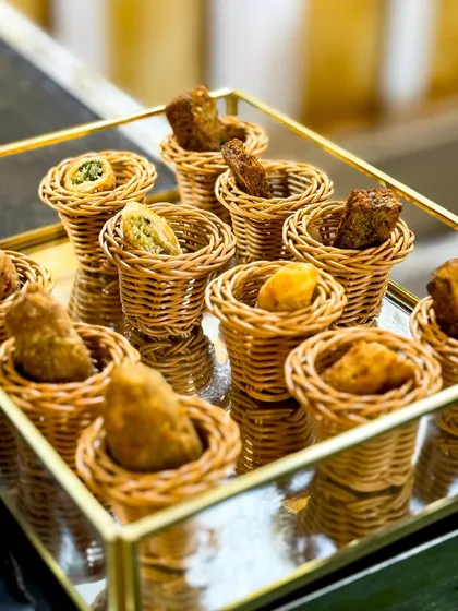 A tray of assorted bite sized appetizers served in cute wicker baskets. This presentation is perfect for pass around service during cocktail hours, offering guests a variety of flavours.