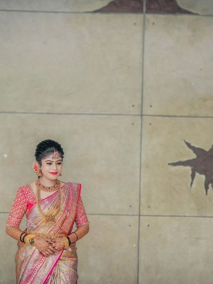 A bridal portrait against a simple wall, making her colorful saree and jewelry the focus.