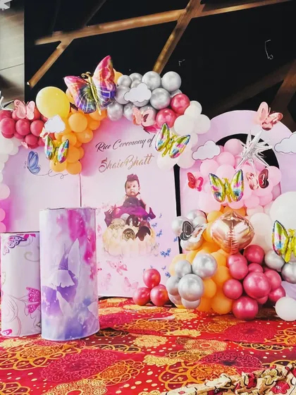A butterfly-themed decoration for a Rice Ceremony. The pink arched panels with the baby's photo and a colorful balloon arch create a lovely and personal backdrop.