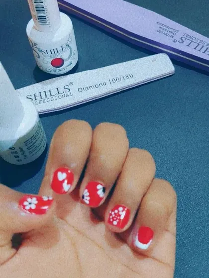 A closer look at some fun, hand-painted nail art on a vibrant red base. This is a great example of how we can personalize your manicure with cute hearts, flowers, and other designs.