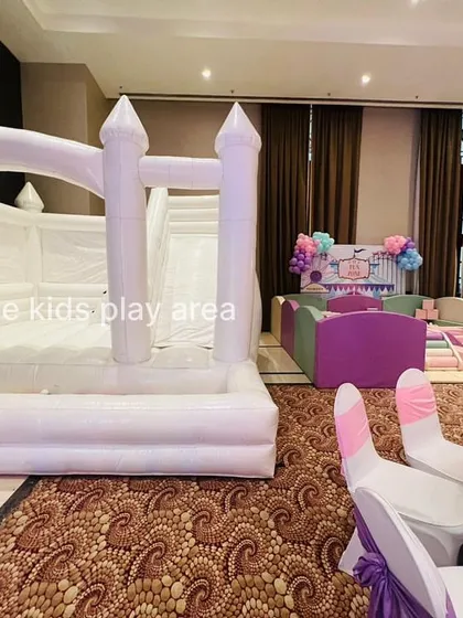 A wide view of an indoor event hall with our white bounce castle and a separate pastel soft play area, creating a dedicated kids' corner.