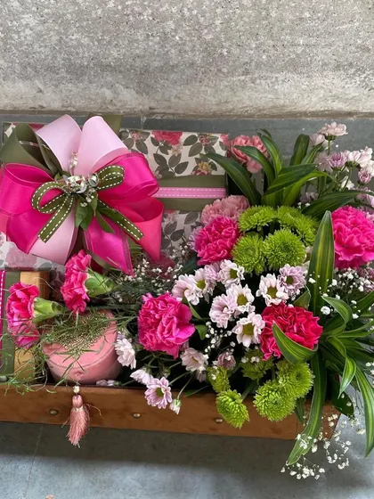 A close-up of a colorful gift hamper, showing the large, vibrant pink bow and the mix of floral-patterned boxes and fresh flowers. This is a perfect gift to express joy and appreciation.