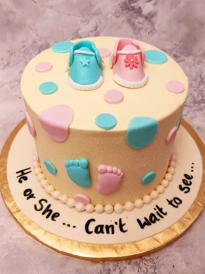 A playful gender reveal cake with pink and blue polka dots, tiny footprints, and baby shoes on top.