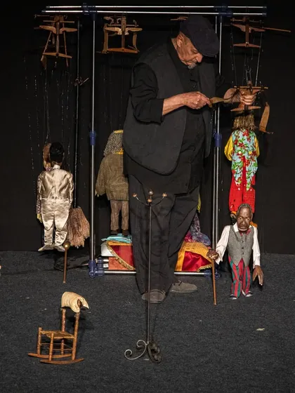 The puppeteer of 'Il Fil'armonico' stands amidst his creations, a master of his craft surrounded by the characters he brings to life.