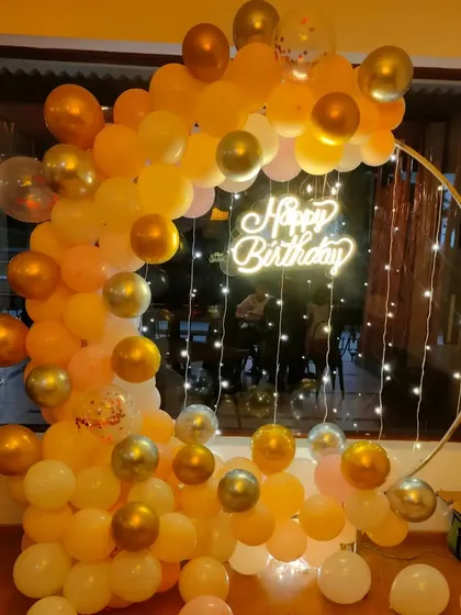 A warm-toned balloon arch in shades of orange and gold with a neon sign and fairy lights, creating a cozy and inviting party backdrop.
