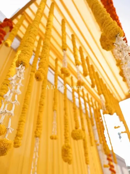 A low-angle shot of hanging marigold garlands against a yellow draped ceiling, creating a traditional and festive look.