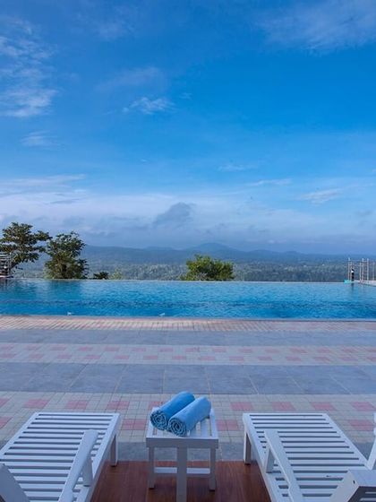 The infinity pool at Coorg Cliffs Resort on a clear day, with the distant mountains visible beyond the blue water.