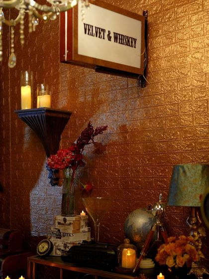 A corner of "The Secret Waltz" speakeasy, featuring a "Velvet & Whiskey" light box sign, textured copper walls, and vintage props that add to the Prohibition-era ambiance.