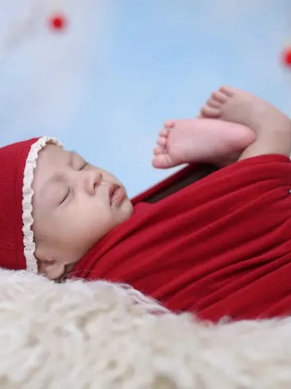 A simple and sweet Christmas pose. The baby is wrapped in red, lying on a soft fur rug against a wintery blue sky backdrop with festive red baubles.