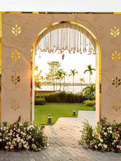 A grand entrance arch designed with peach tones and reflective gold leaf motifs. This elegant doorway, adorned with hanging floral strings, welcomed guests to the garden ceremony with a touch of modern sophistication.