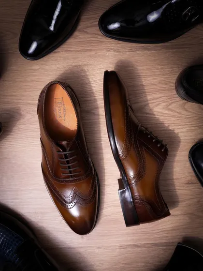 An overhead shot of classic brown and black formal shoes. The composition creates a sense of variety and choice, while the clean lighting on the wood-textured floor adds a touch of class.