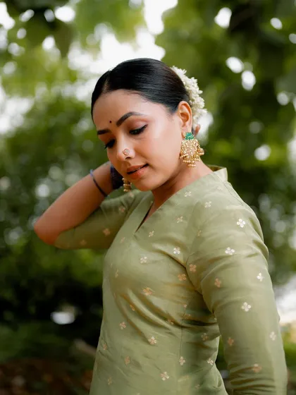 A portrait of actress Anupama Gowda in a simple yet elegant green kurta. The natural, out-of-focus background makes her the clear subject of the image.