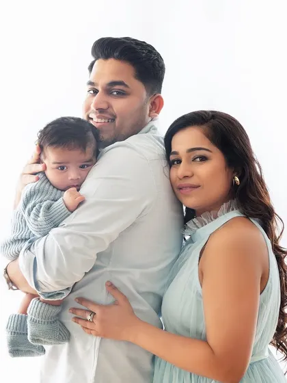 A classic family portrait against a clean, bright background. The coordinated outfits and loving poses create a timeless image for this new family of three.