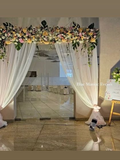 An elegant entrance decoration for an engagement party. The floral arch over the glass doors, paired with a personalized welcome easel, creates a grand and inviting entryway for guests.