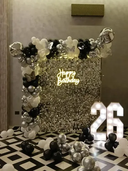 A black and white themed 26th birthday party with a silver sequin wall. The decoration includes a balloon arch and large marquee numbers.
