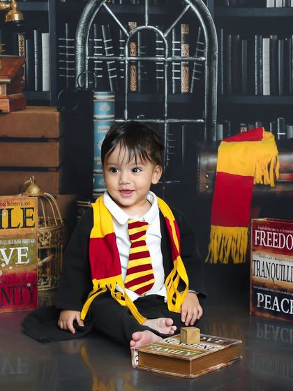 This young wizard is sitting proudly with his Gryffindor scarf. The vintage props and library backdrop add an authentic touch to this magical photoshoot.