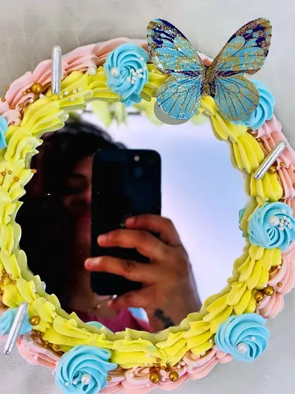 A unique selfie mirror cake. The center of the cake is a real mirror, framed with colorful frosting and a beautiful butterfly, making it a fun and interactive dessert.