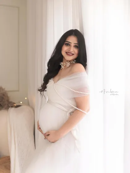 A lovely standing portrait by the window. The natural light beautifully illuminates her, highlighting her pregnancy glow and the delicate details of her gown.