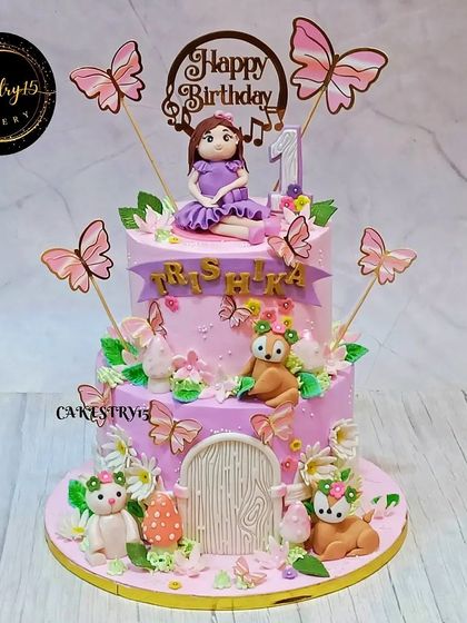 An enchanting two-tier fairy-themed cake for a first birthday. This lavender and pink cake features a fondant fairy, forest critters, and a whimsical fondant door to a magical world.