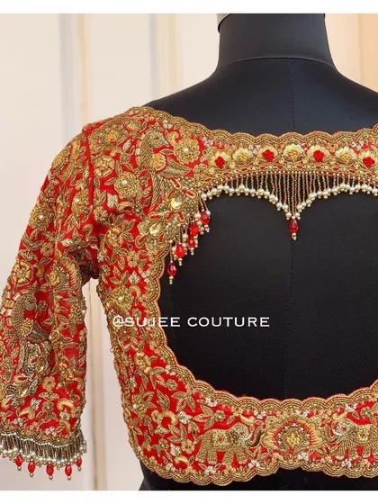 A showcase of one of my signature statement back designs. This vibrant red bridal blouse features a dramatic heart-shaped keyhole cutout, heavily embellished with zardozi work and delicate pearl tassels for a truly memorable look.