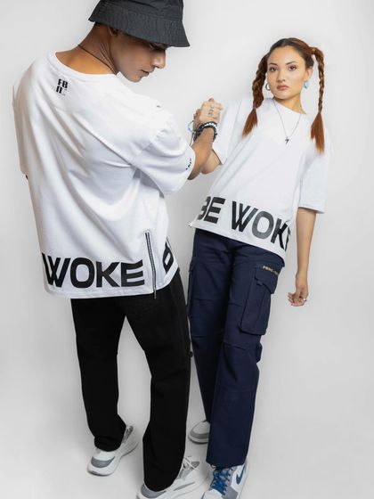 A studio shot for a streetwear brand, focusing on the back and side details of the graphic tees. The pose highlights the zipper detail and bold "WOKE" text.