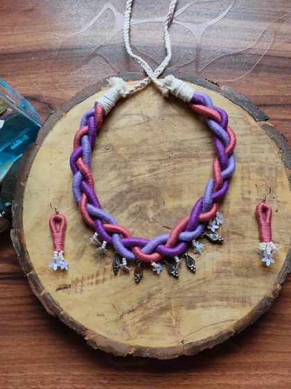 I created this braided thread necklace for a modern, boho look. The shades of purple and pink are woven together and accented with small silver charms, and it comes with matching earrings.