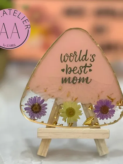 A triangular resin frame in soft pink, decorated with preserved purple flowers. It's a unique shape that makes the "World's Best Mom" message stand out.