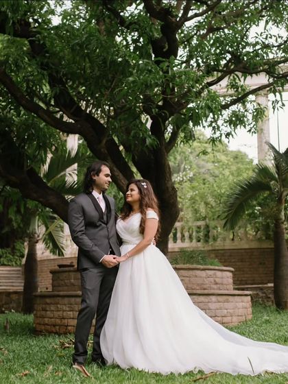 A classic, full-length portrait of the bride and groom in a beautiful garden setting, showcasing the bride's elegant white wedding dress.